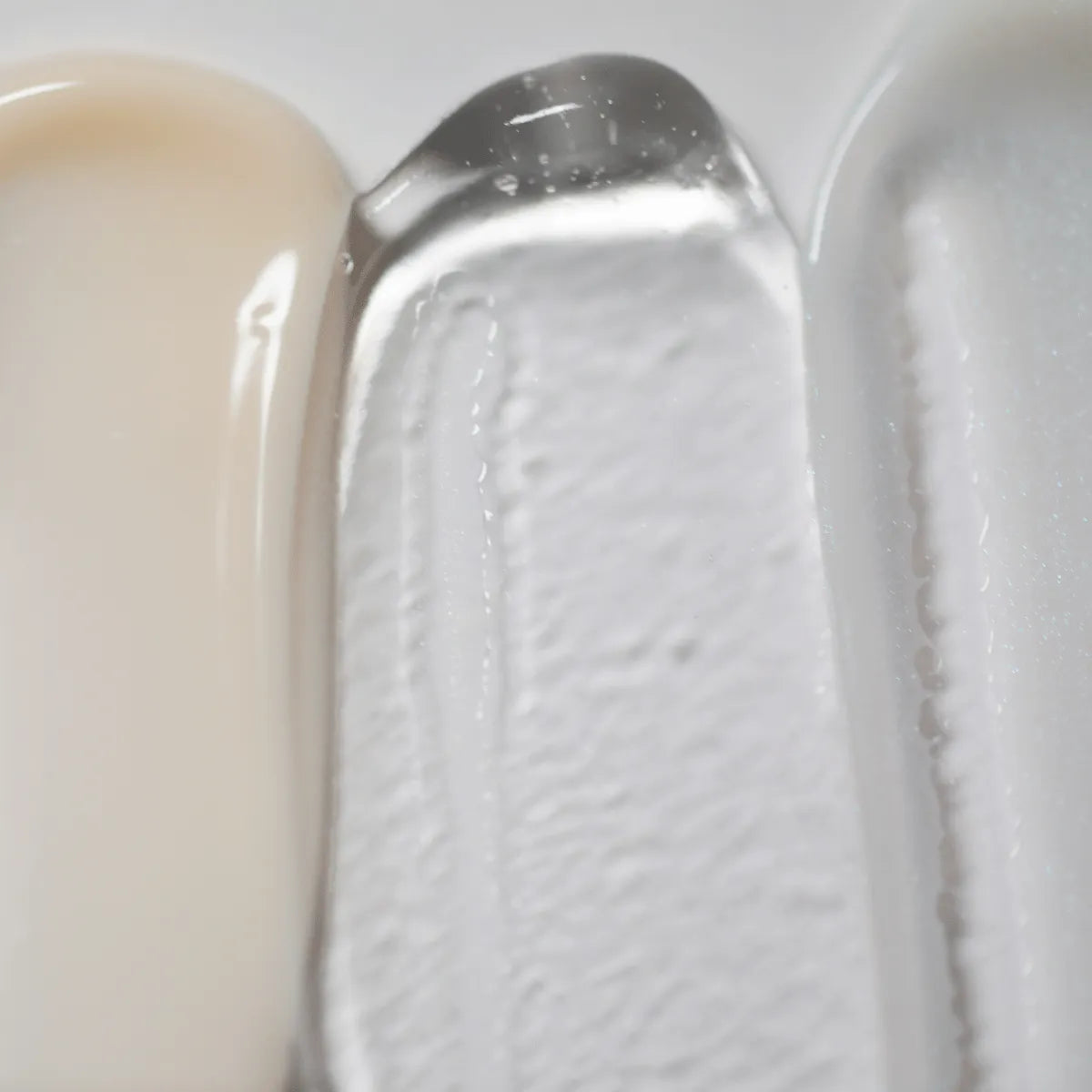 Un'immagine ravvicinata mostra le texture di Solawaves LightBoost Wand Activating Serum, con il beige cremoso, il gel trasparente infuso con la tecnologia LightBoost e la crema liscia grigio chiaro/bianco. Le texture variano da cremose a gel, ognuna delle quali presenta una finitura lucida.